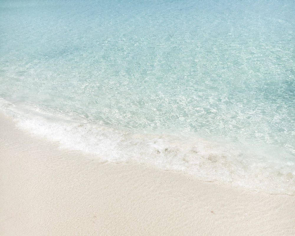 Crystal clear waves coming in on a white sandy beach.