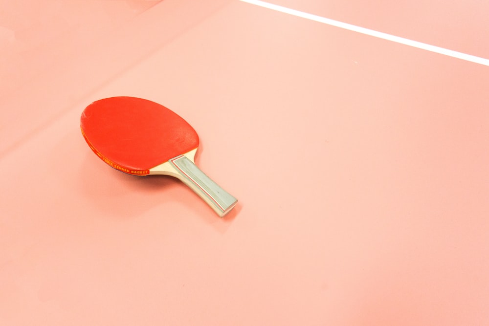 A red table tennis paddle sitting on a court.