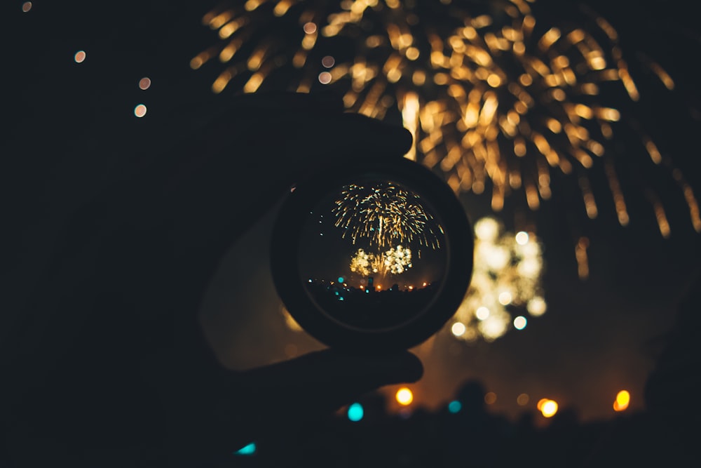 a person holding a glass ball with fireworks in the background