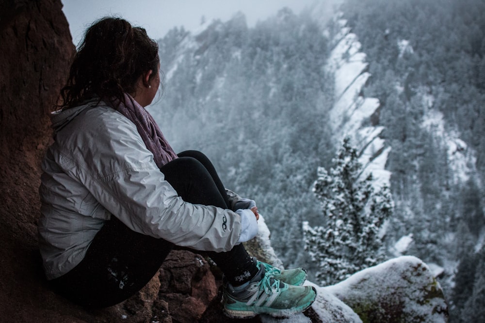 woman sitting on rock formation under snow