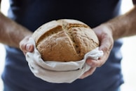 A friendly artisan handing a freshly baked loaf of bread to a customer wrapped in soft tan paper.