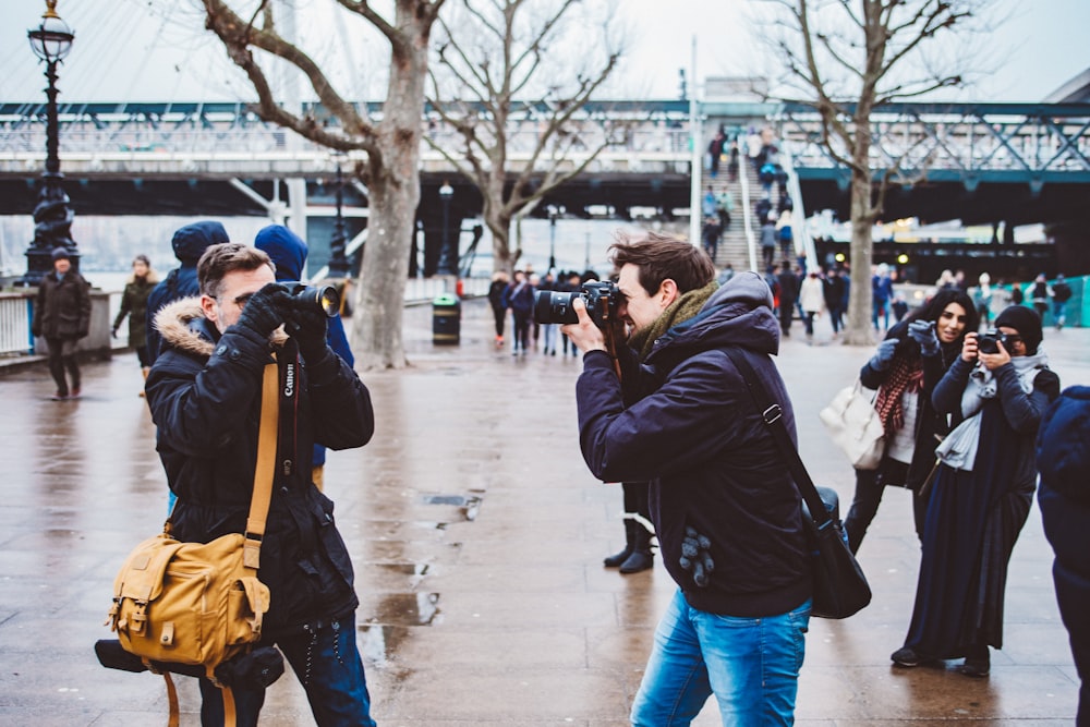 two men facing each other taking photo in black DSLR camera during daytime