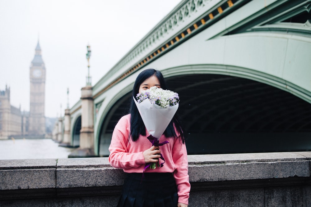 Femme tenant un bouquet de fleurs debout à côté de balustrades en béton