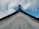 A traditional architectural roof with ornate patterns exists against a backdrop of a partly cloudy sky. The roof features a decorative edge with subtle red and gold detailing, and the tip slightly curves upward.