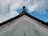 A traditional architectural roof with ornate patterns exists against a backdrop of a partly cloudy sky. The roof features a decorative edge with subtle red and gold detailing, and the tip slightly curves upward.