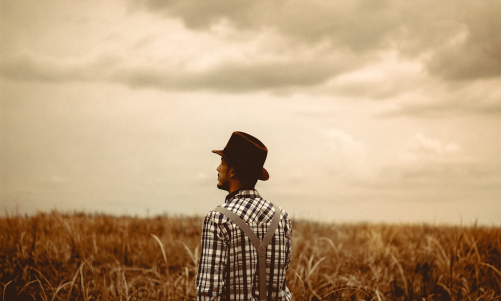 Hombre con sombrero negro de pie en el campo marrón durante el día