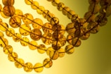 Several strings of round amber beads are intertwined, displaying varying translucency and subtle inclusions. The beads exhibit a rich, warm golden hue with visible dark specks inside each sphere.