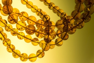 Several strings of round amber beads are intertwined, displaying varying translucency and subtle inclusions. The beads exhibit a rich, warm golden hue with visible dark specks inside each sphere.