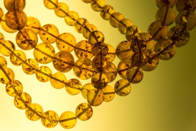 Several strings of round amber beads are intertwined, displaying varying translucency and subtle inclusions. The beads exhibit a rich, warm golden hue with visible dark specks inside each sphere.