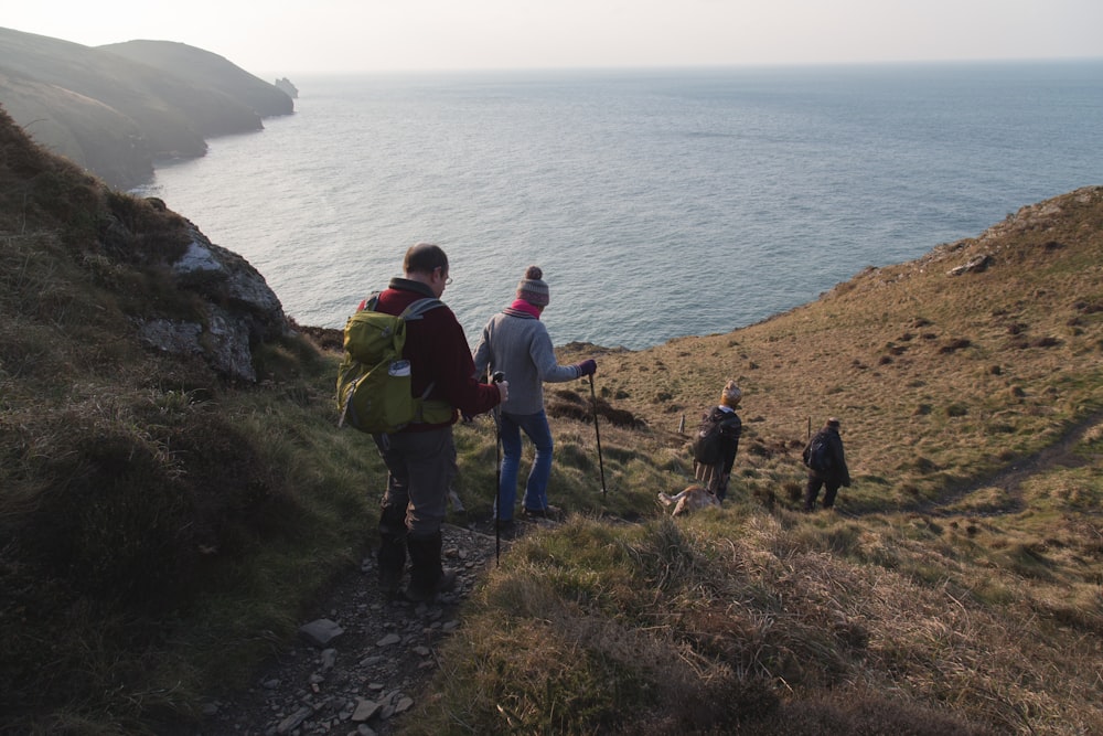 four hiking on mountain viewing blue sea during daytime