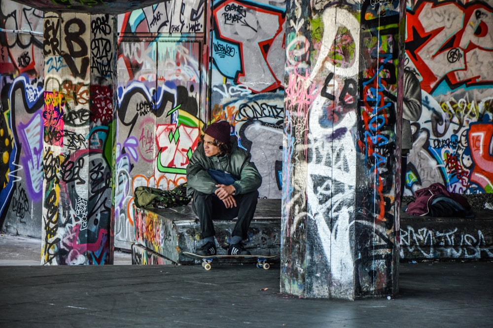 man wearing green jacket sitting with skateboard