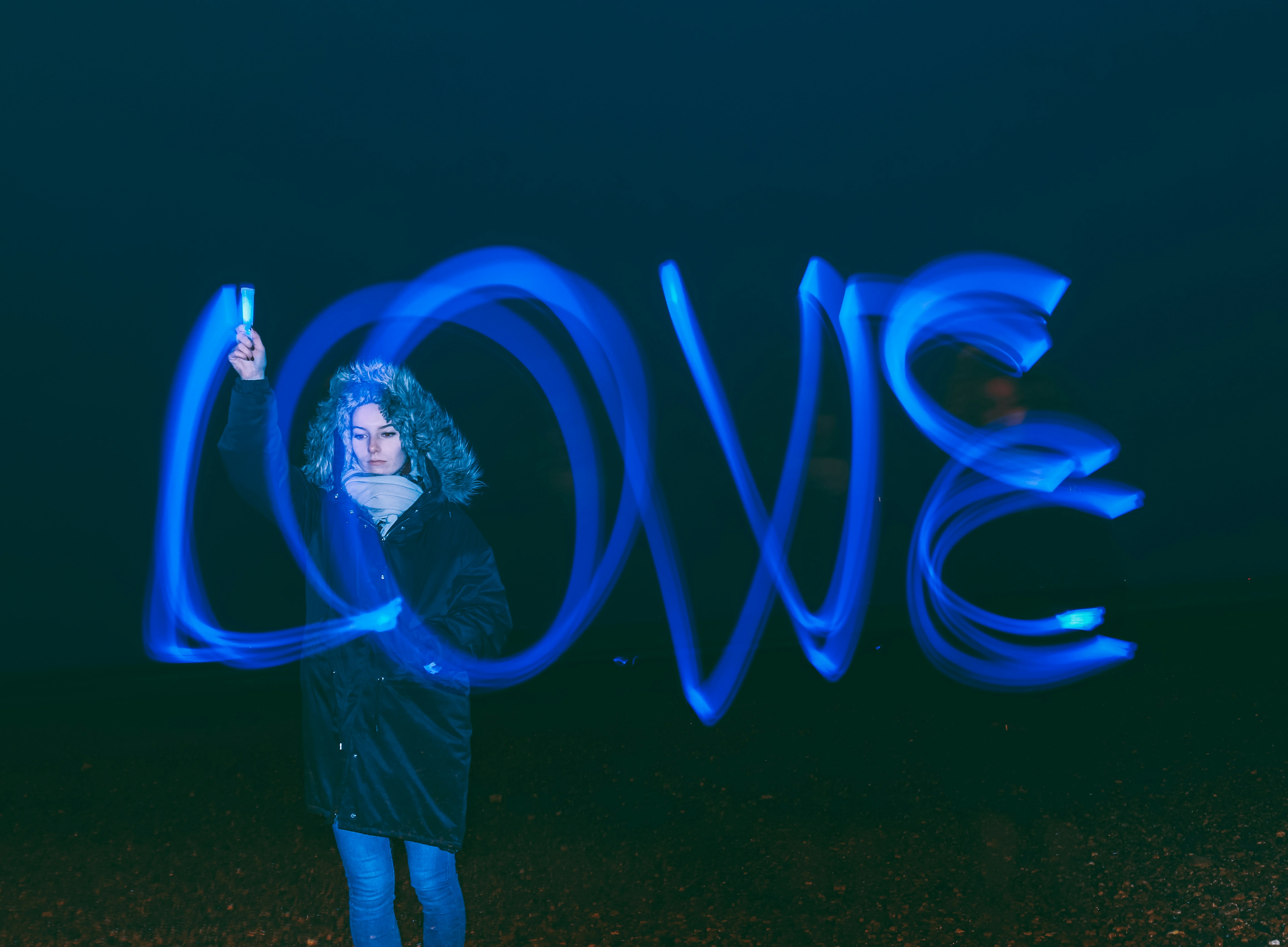 high exposure photo of standing woman writing love word in the air using blue light pen