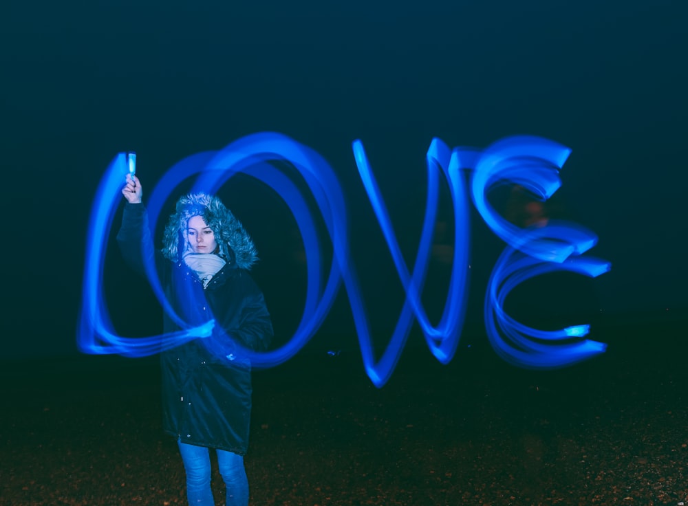 high exposure photo of standing woman writing love word in the air using blue light pen