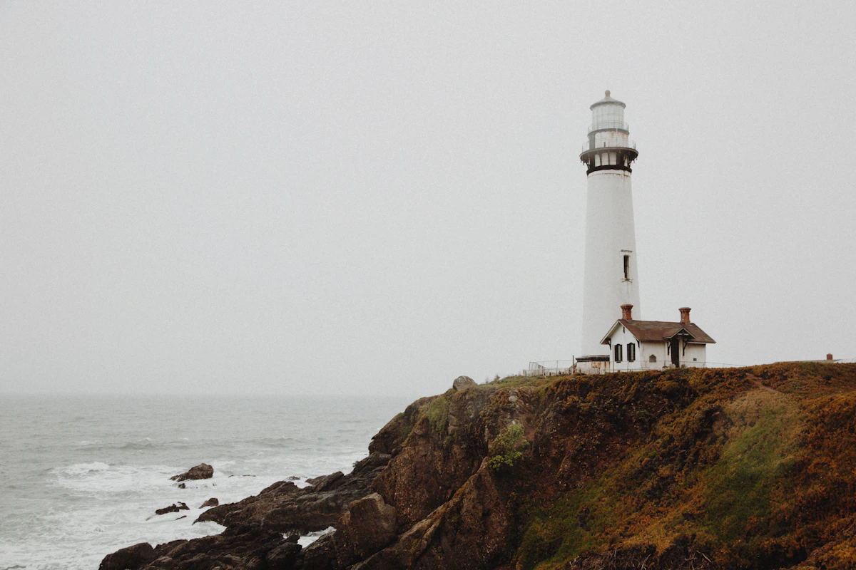 A solitary lighthouse on a rocky headland in coastal fog