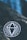 A black circular sticker with a white geometric diamond design placed on a rough, dark stone surface. The background features a blurred blue area, possibly indicating water or sky, with some small, scattered leaves.