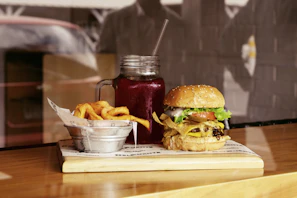 A rustic wooden table with a burger, crispy fries, and a cold drink by the seaside terrace