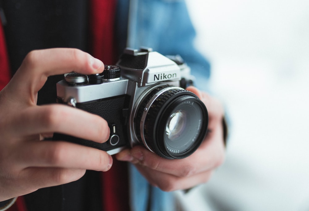 personne tenant un appareil photo reflex numérique Nikon noir et gris