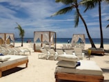 Massage beds under a bright blue canopy on a sunny beach with ocean waves in the background