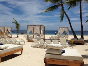 Massage beds under a bright blue canopy on a sunny beach with ocean waves in the background