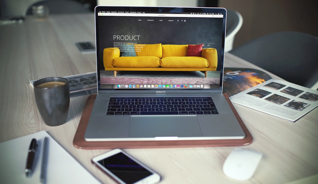 A Macbook on a wooden surface with a smartphone, a cup of coffee and an open booklet