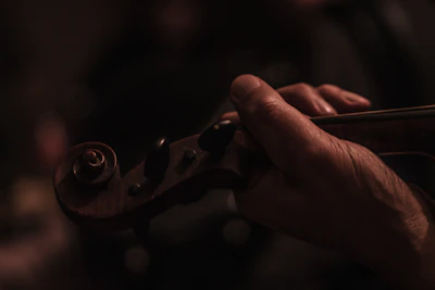 Close-up of hands gently holding violin bow over sheet music with bright, warm tones.