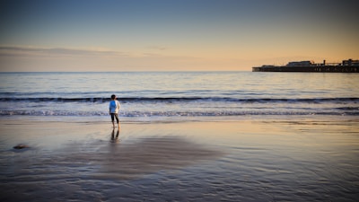 A calm child sitting on the beach at sunset, feeling the gentle sea breeze and soft sand.