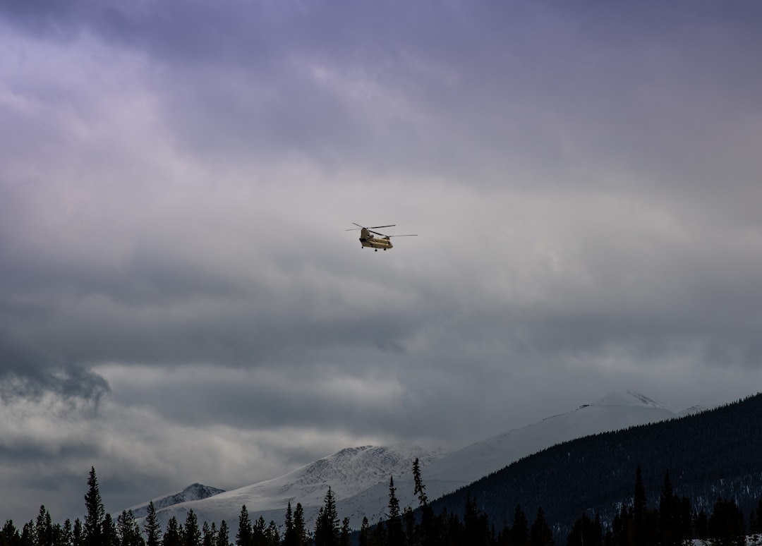 brown helicopter flying under cloudy sky,