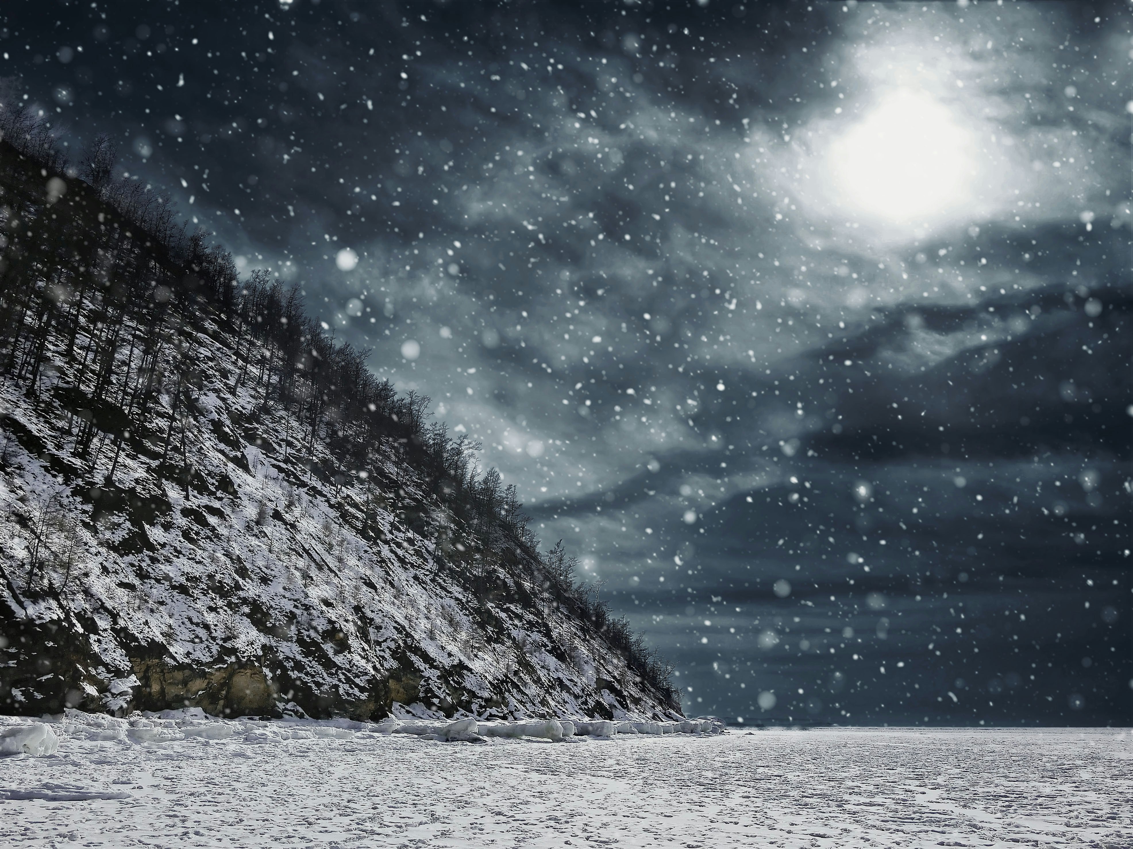 Snowing in a cloudy night sky on a grassy mountain.