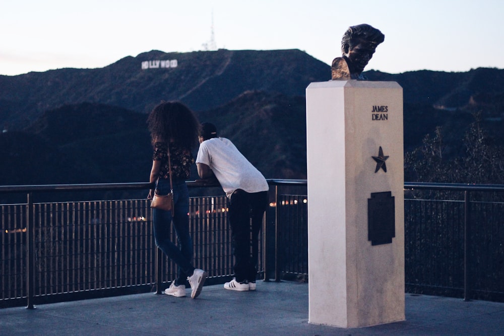 two man and woman leaning on railing and Hollywood Sign at the distance during day
