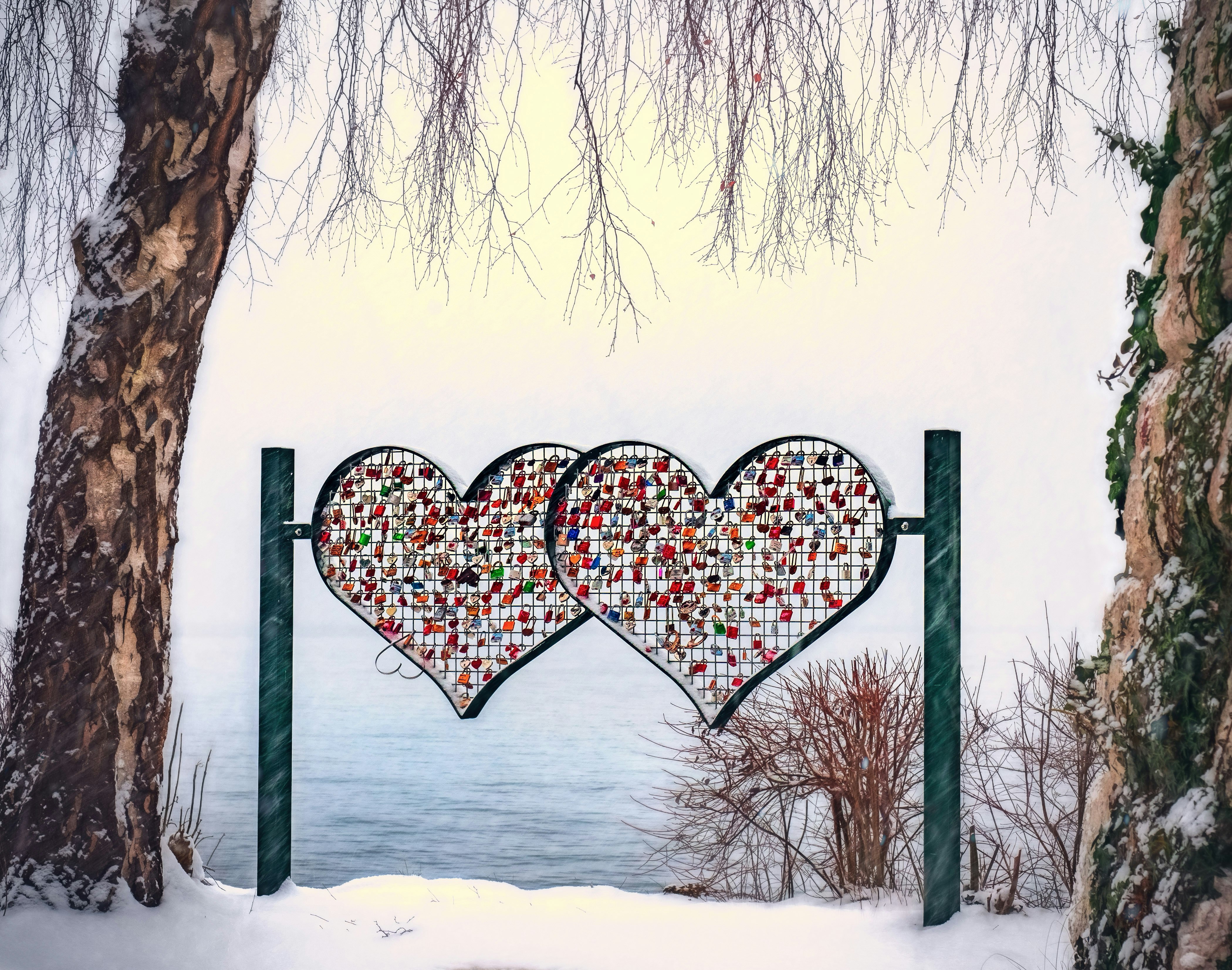 Two colorful heart shapes hanging from poles in front of the water.