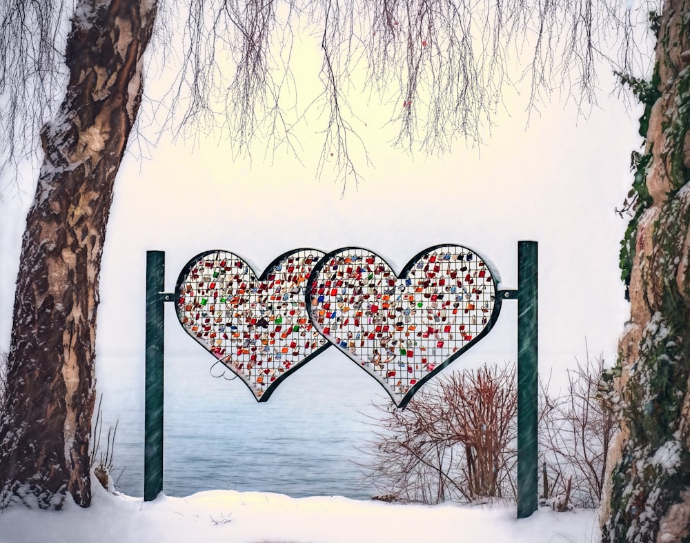 Two colorful heart shapes hanging from poles in front of the water.