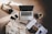 A cozy flat lay featuring a laptop, two smartphones, a camera, a pair of glasses, a magazine, a hot beverage in a mug, and a fringed blanket spread out on a carpet. The items are arranged in a relaxed, casual manner, suggesting a comfortable work or leisure setting.