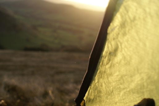 A close-up shot of a sunlit tent fabric with a blurred background of a hilly landscape bathed in soft, warm light.