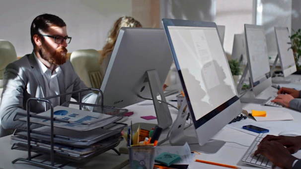 Rows of computer stations with employees focused on their screens in a bright workspace.