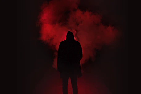 Cinematic shot of oversized black hoodie with glowing red angel wing embroidery against a smoky black gradient background.