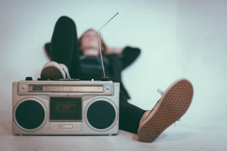A person in sneakers resting feet on a vintage silver boombox