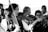 A group of musicians is gathered, with a woman in traditional clothing playing a violin. Her hair is adorned with a flower, and she exhibits a focused expression. Other musicians are in the background, playing string instruments.