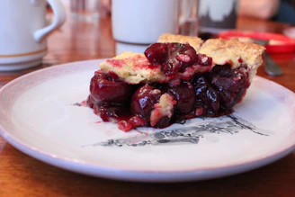Close-up of a slice of cherry pie with juicy filling oozing out and a dollop of whipped cream.