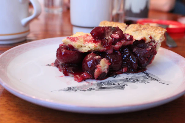 Close-up of a slice of cherry pie with juicy filling oozing out and a dollop of whipped cream.