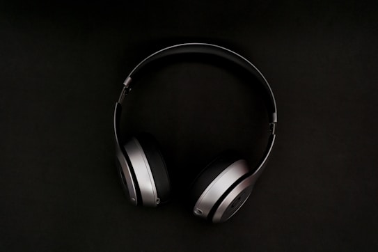 A pair of sleek, modern headphones with a metallic finish and cushioned ear pads, set against a dark background.