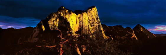 Dramatic mountain runner at dawn on a rugged trail in Sierra Blanca, with dark skies and orange-golden light highlighting the terrain.