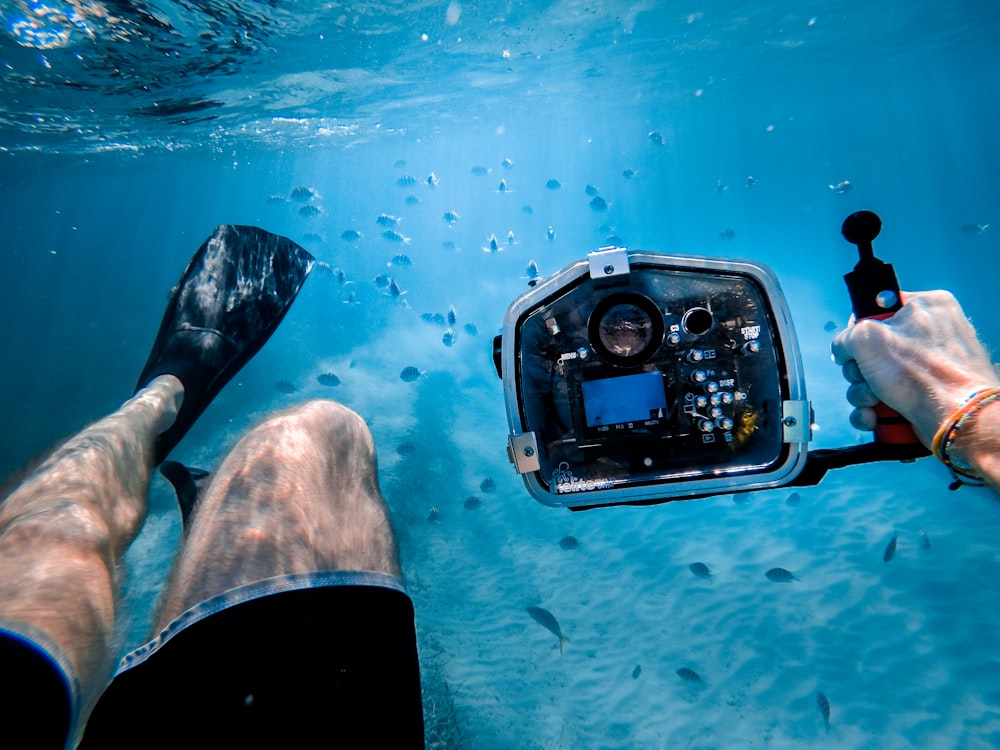 hombre bañándose bajo el mar mientras sostiene una cámara negra