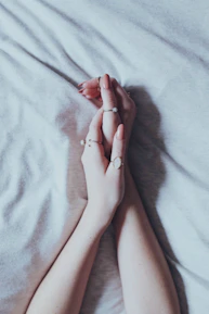 Elegant hands wearing layered rings against a muted pastel background.