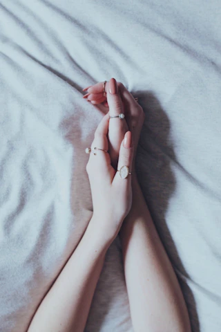 Elegant hands wearing layered rings against a muted pastel background.