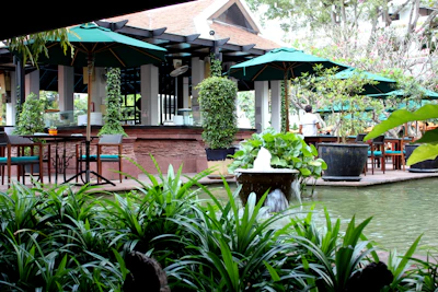 A serene outdoor patio with comfortable seating surrounded by lush greenery and soft lantern lighting.