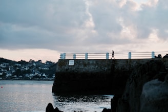 Moody nighttime shot of a lone figure walking along a rain-slicked urban pier.