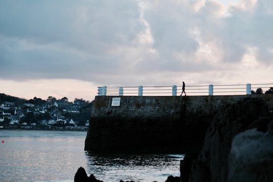 Moody nighttime shot of a lone figure walking along a rain-slicked urban pier.