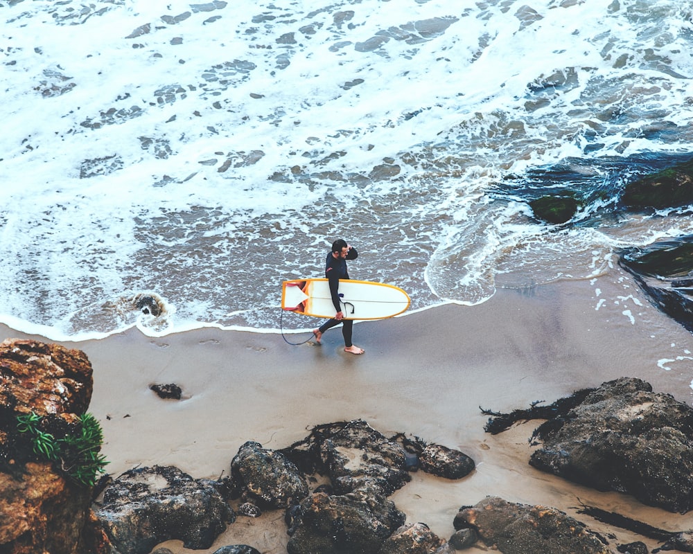 uomo che tiene la tavola da surf che cammina in riva al mare durante il giorno