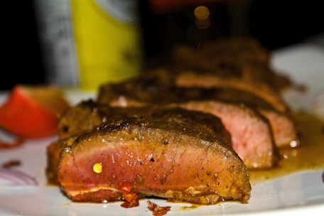 A close-up of a chef’s hands plating a perfectly cooked, juicy steak garnished with spices.