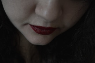 A close-up of a woman applying lipstick in a soft-lit setting.